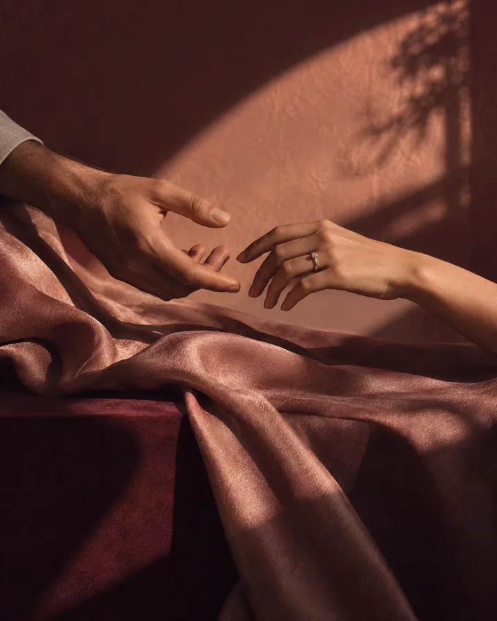 Two hands reaching across rose silk in afternoon light