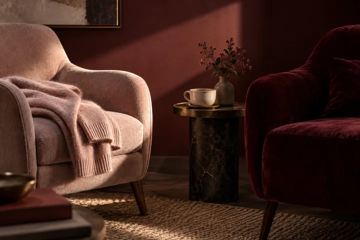 A blush chair and a burgundy chair face each other across a small table with tea
