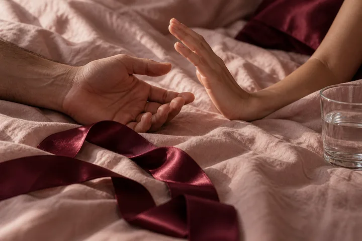 One open hand meets another raised hand across pale bedding, with a burgundy ribbon between them.