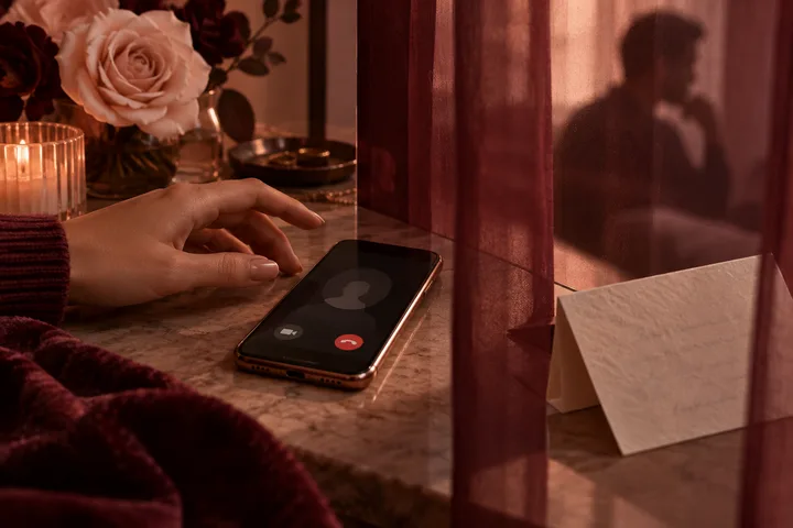 A hand reaches toward a phone showing a blurred caller, beside sealed envelopes, roses, and a key.